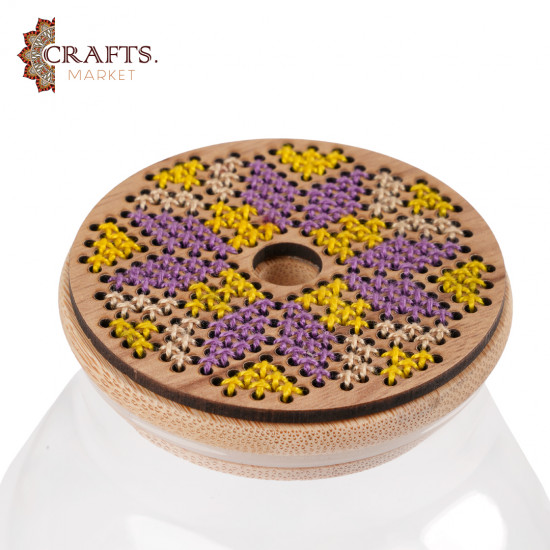 A glass container with a wooden lid, decorated with hand-embroidered rural geometric patterns