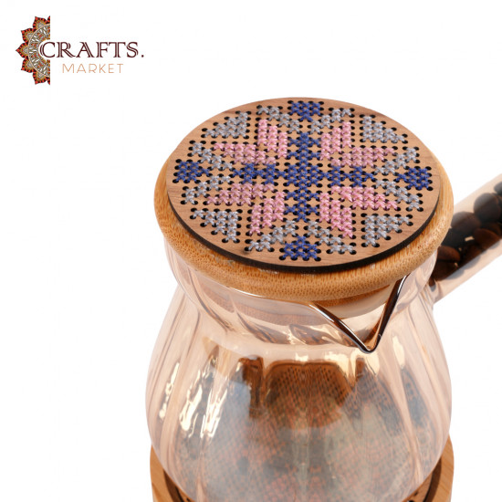 A glass coffee pot with a hand-embroidered wooden lid and a hand-embroidered wooden coaster